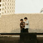 Two boys standing on a roof looking at a cell phone